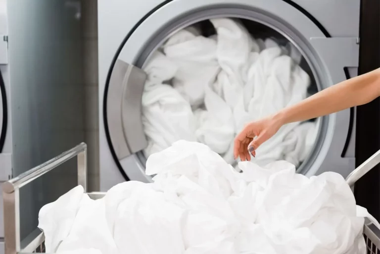 Hand entnimmt frisch gewaschene Hotelwäsche aus einer Industriewaschmaschine